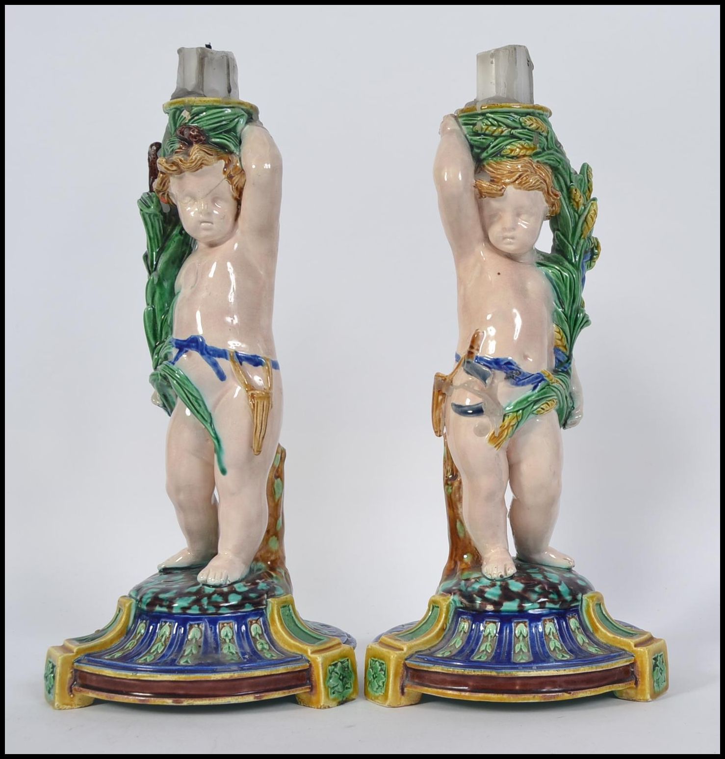 A pair of Minton Majolica figural candlesticks modelled as cherubs raised on naturalistic socle