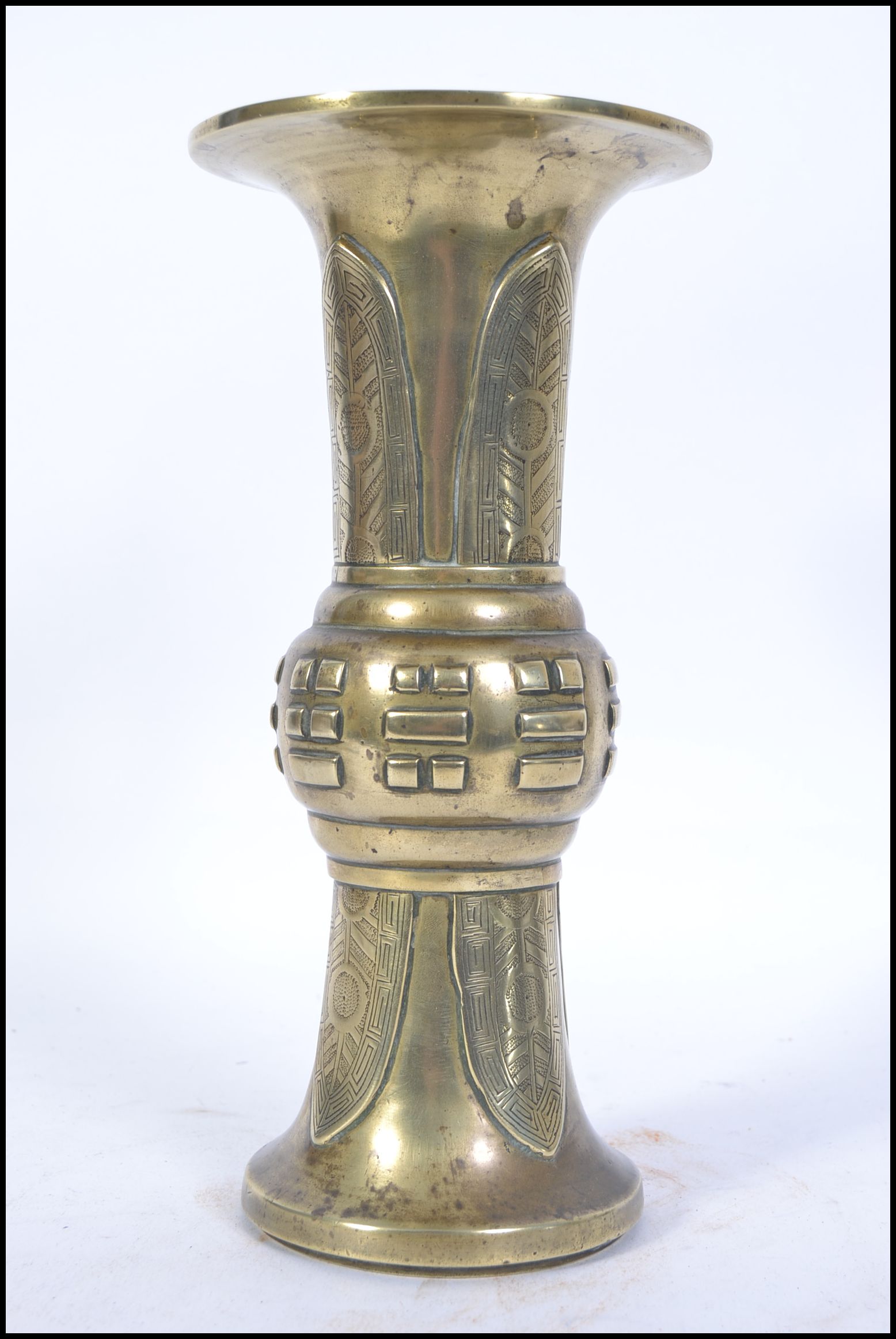 A Chinese brass gu vase of cylindrical form with geometric designs and symbols,