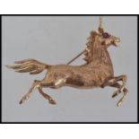 A stunning 9ct gold brooch in the form of a running horse having garnet stone eyes complete with