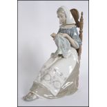 A large Lladro figurine of a seated lady sewing a tapestry.