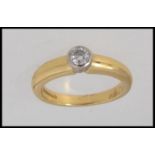 An 18ct gold ring set with central round cut solitaire diamond in a rub over setting.