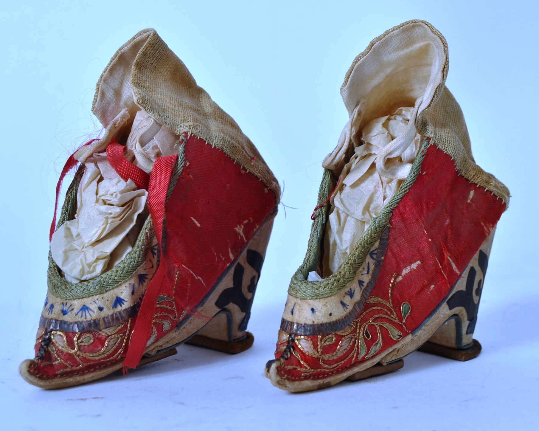 A pair of Chinese red silk and embroidered shoes with laces being handstitched,