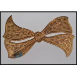 A 1920s vintage gold tone brooch in the shape of a bow with embossed foliate decoration.