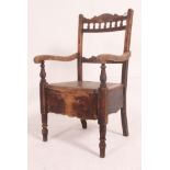 A Victorian commode chair in oak being raised on turned legs having a hinged seat with decorative