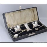A cased silver hallmarked condiment set comprising lidded pot and open pot,