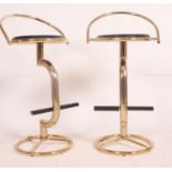 A pair of retro style gilt bar stools, having black circular seat pads and raised foot rests.