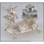 A silver plated desk set, having a pen holder in the form of a cherub playing a string instrument,