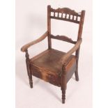 A Victorian commode chair in oak being raised on turned legs having a hinged seat with decorative