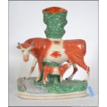 A mid 19th century Staffordshire spill holder in the form of a cow with calf decorated in orange,