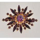 A large 1950s to 1960s amethyst colour rhinestone brooch in a gold tone setting with a roll over