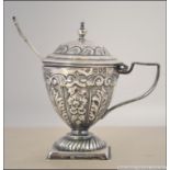 A silver hallmarked mustard pot and spoon in the form of a trophy urn in the rococo style.