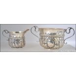 A silver hallmarked Victorian twin handled sugar bowl and creamer cast in relief with rococo scroll