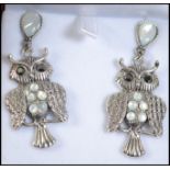 A pair of silver and moonstone adorned earrings in the form of a pair of owls.