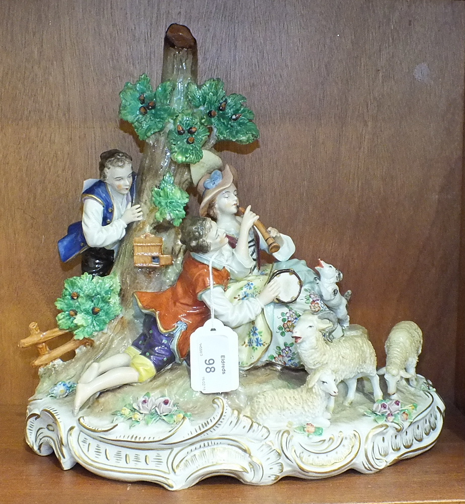 A large Sitzendorf figure group depicting a courting couple sitting beside a tree, she playing a