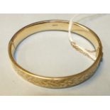 A 9ct gold hinged bangle with engraved floral decoration, 12.3g.