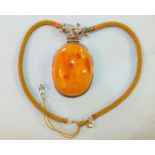 A large butterscotch amber pendant mounted in white metal on plaited necklet with white metal floral