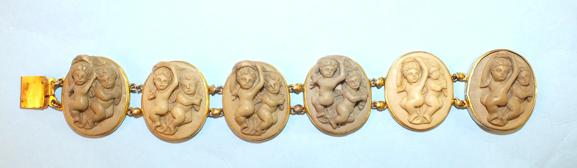 A 19th century lava bracelet of six plaques, each carved in high relief with two infants, in gilt