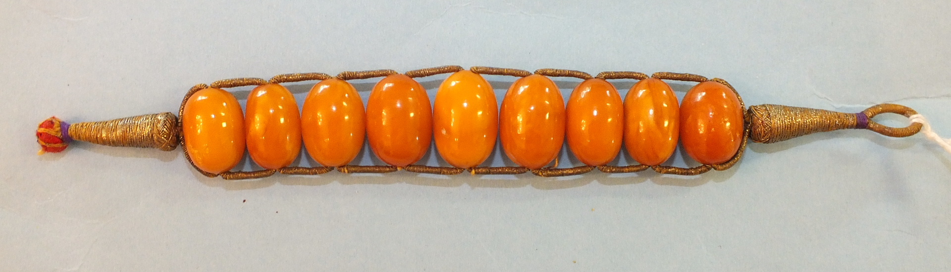An ethnic amber bracelet of nine graduated amber beads on metallic thread mount, 17cm, 16.7g.
