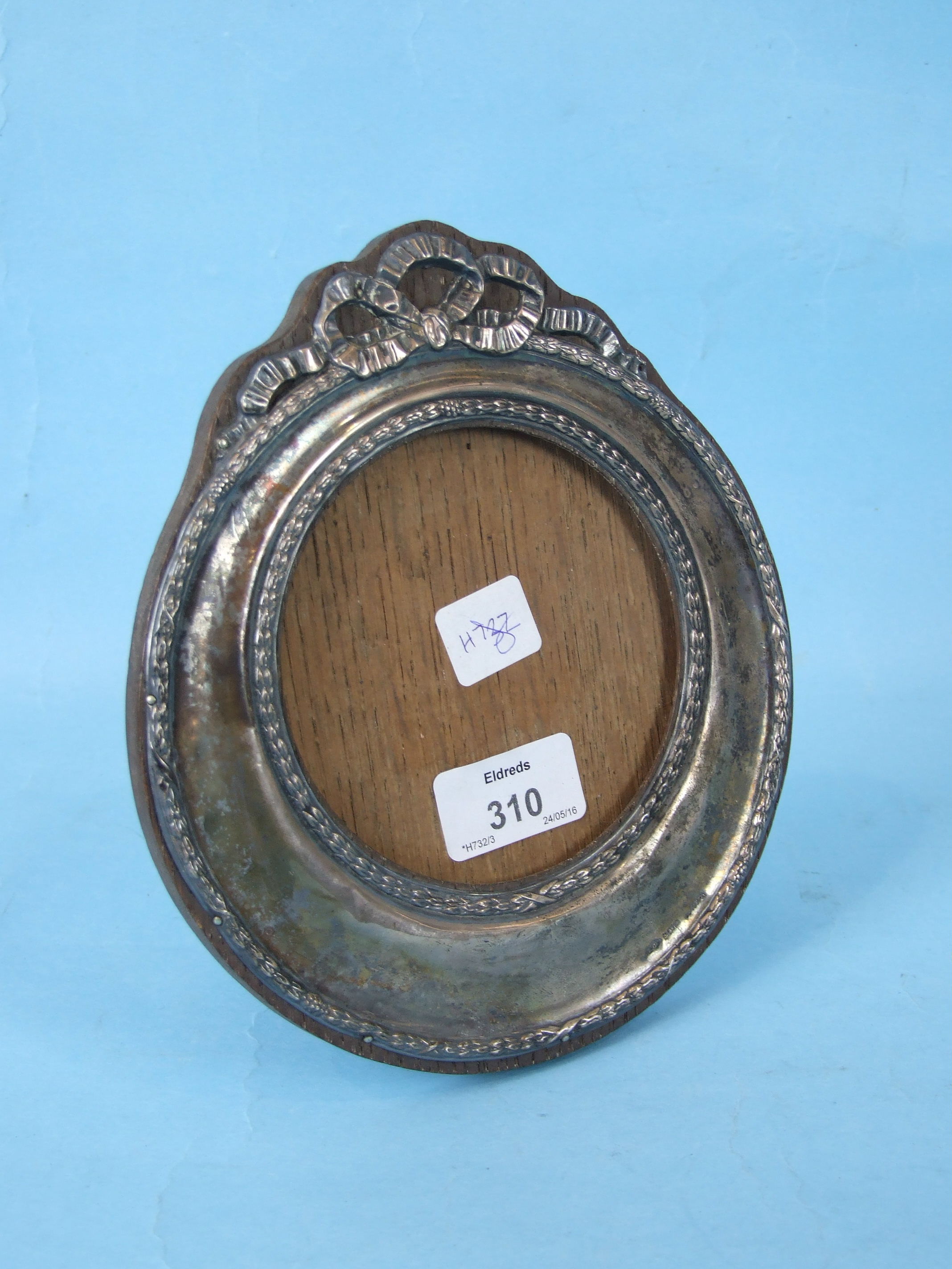 A silver circular photograph frame decorated with raised husk borders and surmounted by ribbons.