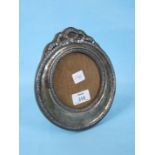 A silver circular photograph frame decorated with raised husk borders and surmounted by ribbons.