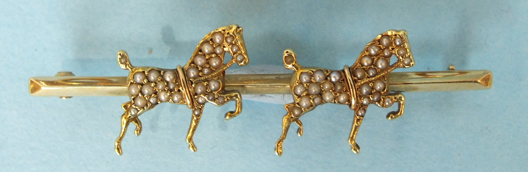 A 14ct gold bar brooch modelled as two prancing horses, each set with seed pearls, 5.2cm long, 5g.