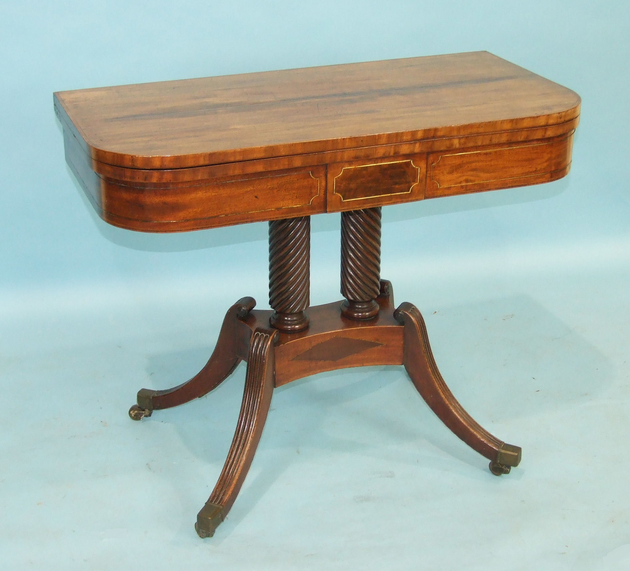 A Regency mahogany fold-over card table, the baize-lined top above a brass-inlaid frieze, raised