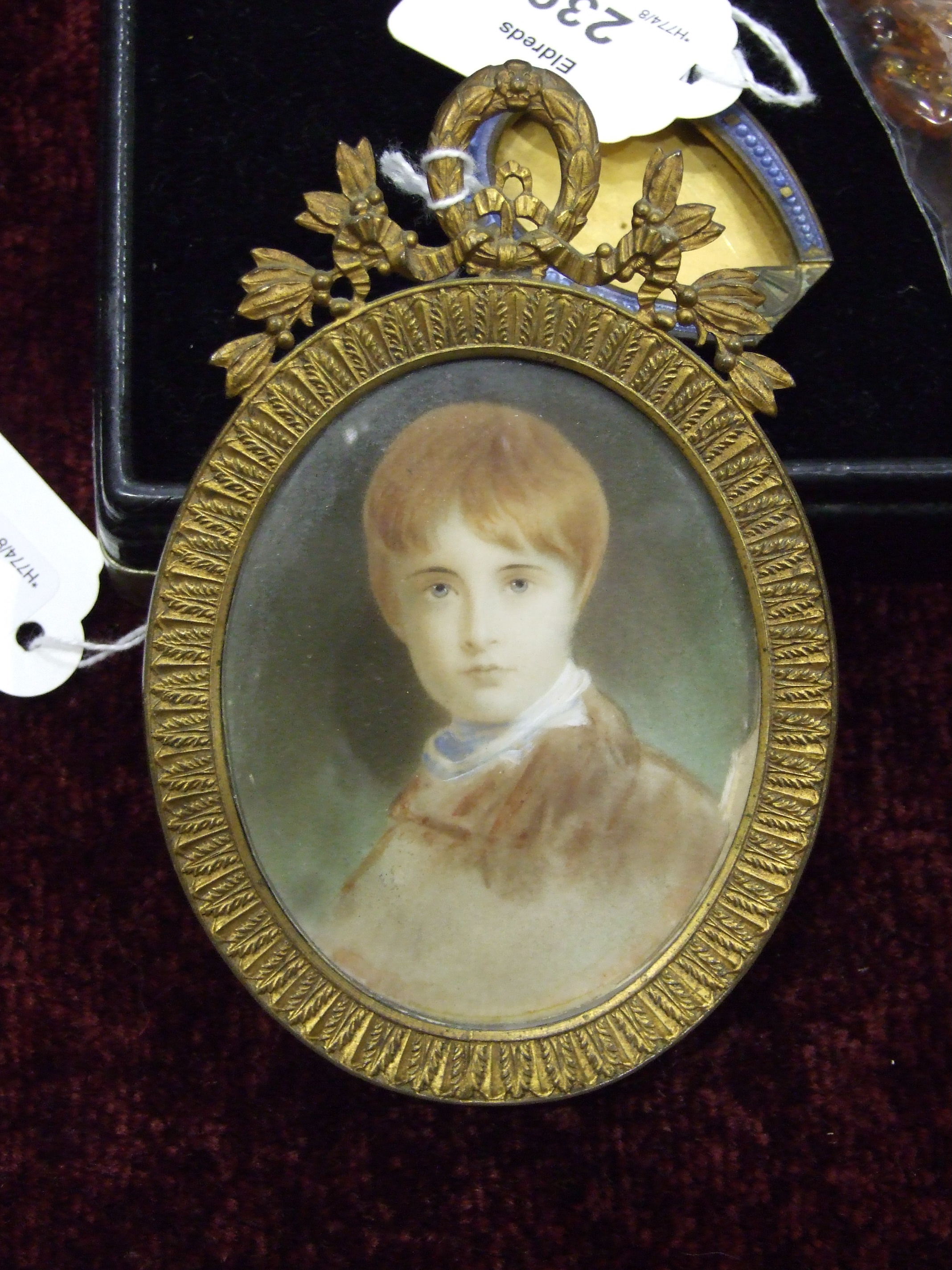 An early 20th century watercolour miniature of a young boy in gilt metal oval strut frame, 13 x