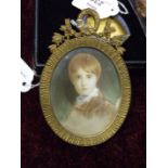 An early 20th century watercolour miniature of a young boy in gilt metal oval strut frame, 13 x