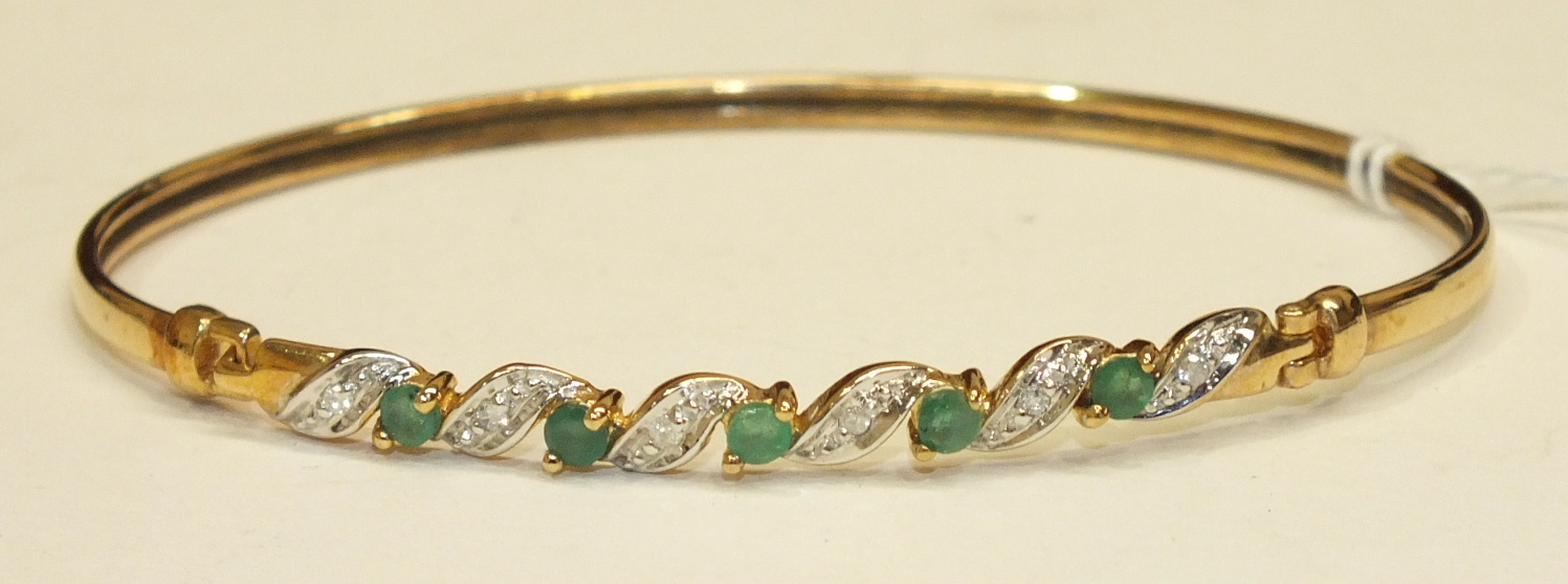 A 9ct gold bangle set five round-cut emeralds with diamond points between, 4.6g, cased.