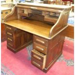 An early-20th century oak knee-hole roll-top desk, revealing pigeon holes and drawers.