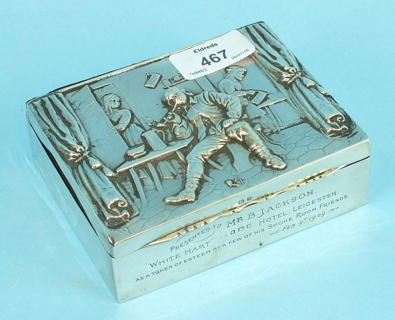 An embossed cigarette box decorated with a tavern scene, presentation inscription to 'Mr B