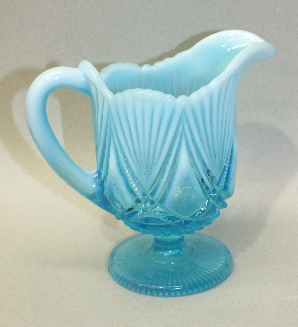 A blue pearline glass cream jug with moulded decoration, raised on a circular foot, possibly by