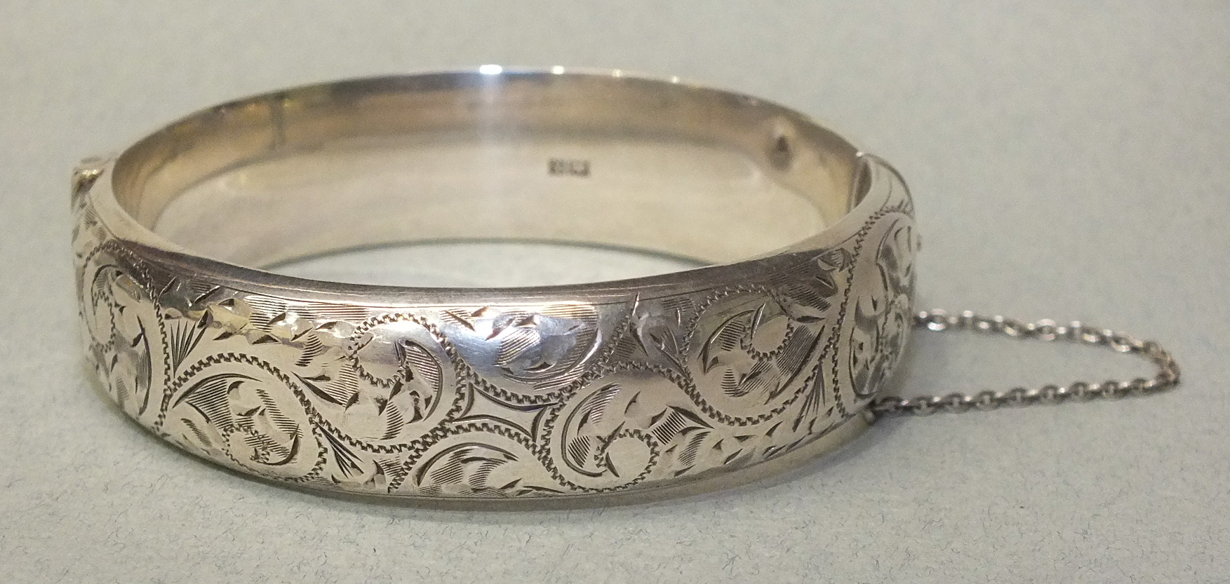 A silver hinged bangle with engraved scroll decoration, Birmingham 1959, 25.5g, (dents).