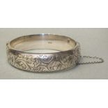 A silver hinged bangle with engraved scroll decoration, Birmingham 1959, 25.5g, (dents).