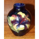 A small Moorcroft baluster-shaped vase decorated with hibiscus flowers on a dark blue ground,
