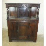 An antique oak court cupboard, the upper part with panelled door and hood supported on turned