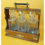 An Edwardian oak Tantalus with plated mounts, the sliding bottle holder with three replaced