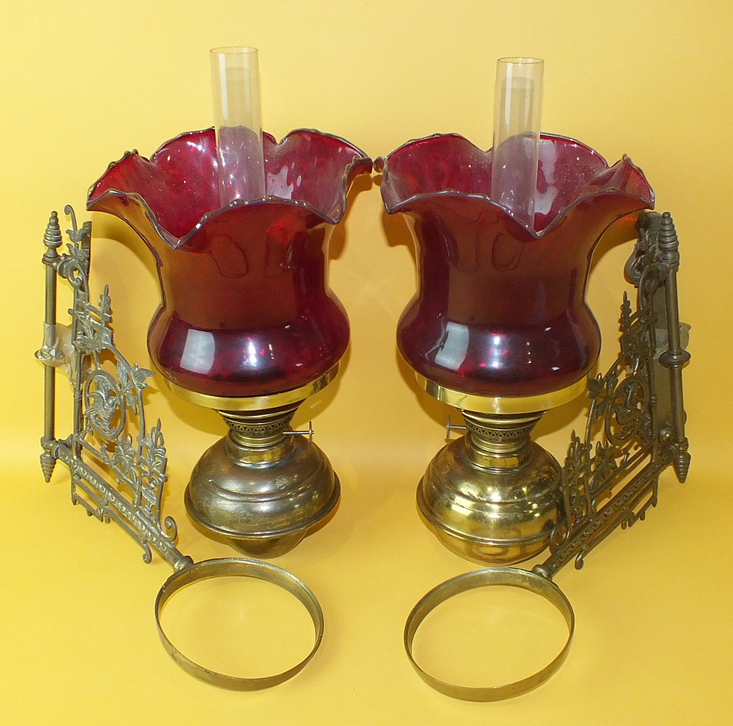 A pair of Edwardian brass bracket-mounted oil lamps with ruby glass shades, (2).