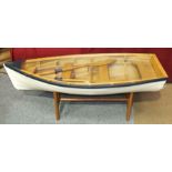 A painted wood model of a clinker-built rowing boat, with oars and plate glass table top, 121cm