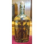 A Folk Art devotional bottle containing carved tools and a cross, preserved in liquid, 24cm high and