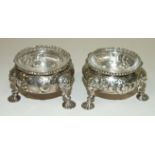 A pair of George II silver salts with embossed floral motifs and gadrooned rim, on three shell feet,