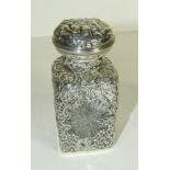 An Edwardian scent bottle of square form, the cut glass flask within pierced and embossed silver