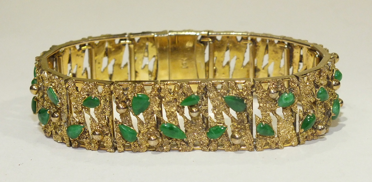 A 14k yellow gold bracelet of textured and pierced linked plaques, each set with two jade cabochons,