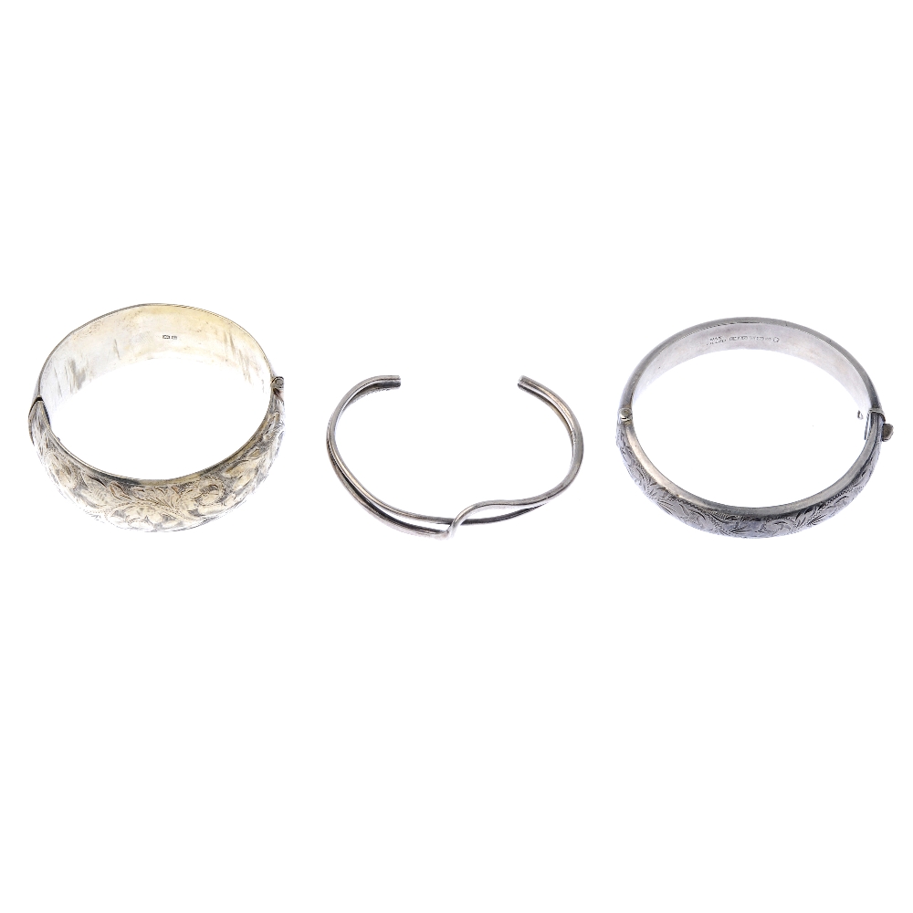 A selection of silver bangles. The first designed as a wide hinged silver bangle with foliate