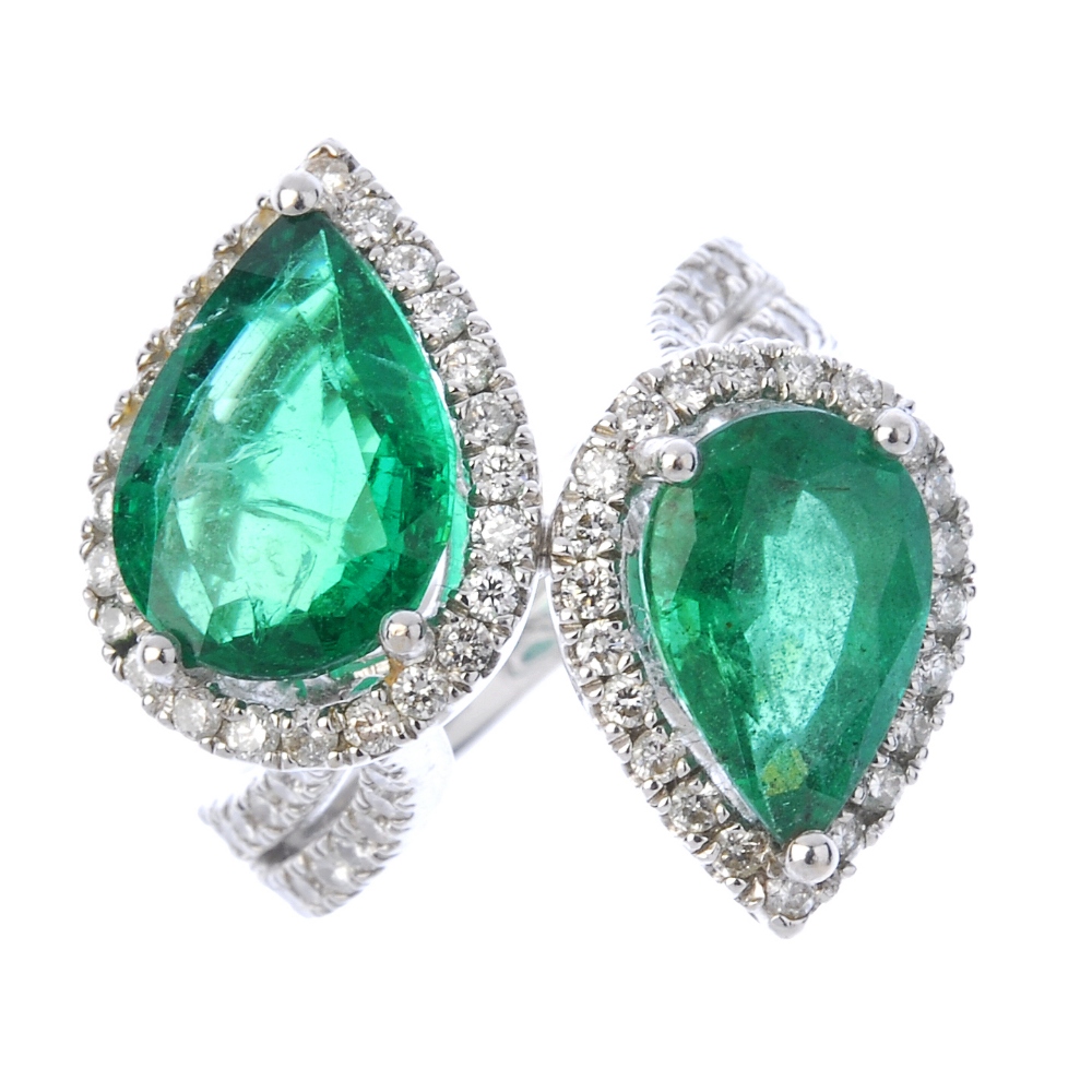 An emerald and diamond crossover ring. Designed as two graduated pear-shape emeralds, each within