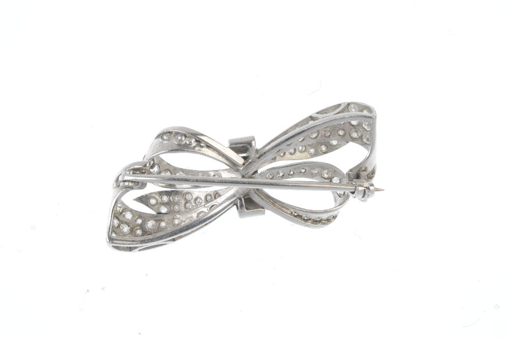 A diamond bow brooch. The brilliant and circular-cut diamond bow, gathered by a tapered baguette-cut - Image 2 of 2
