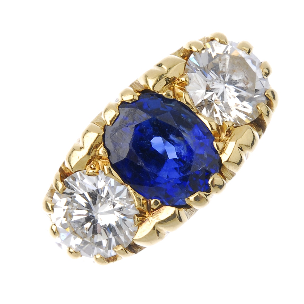 An 18ct gold sapphire and diamond three-stone ring. The oval-shape sapphire, between brilliant-cut