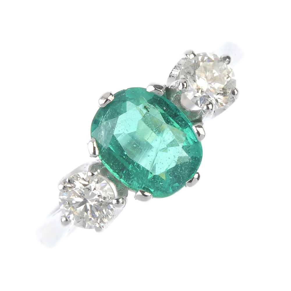 An emerald and diamond three-stone ring. The oval-shape emerald, with brilliant-cut diamond sides,