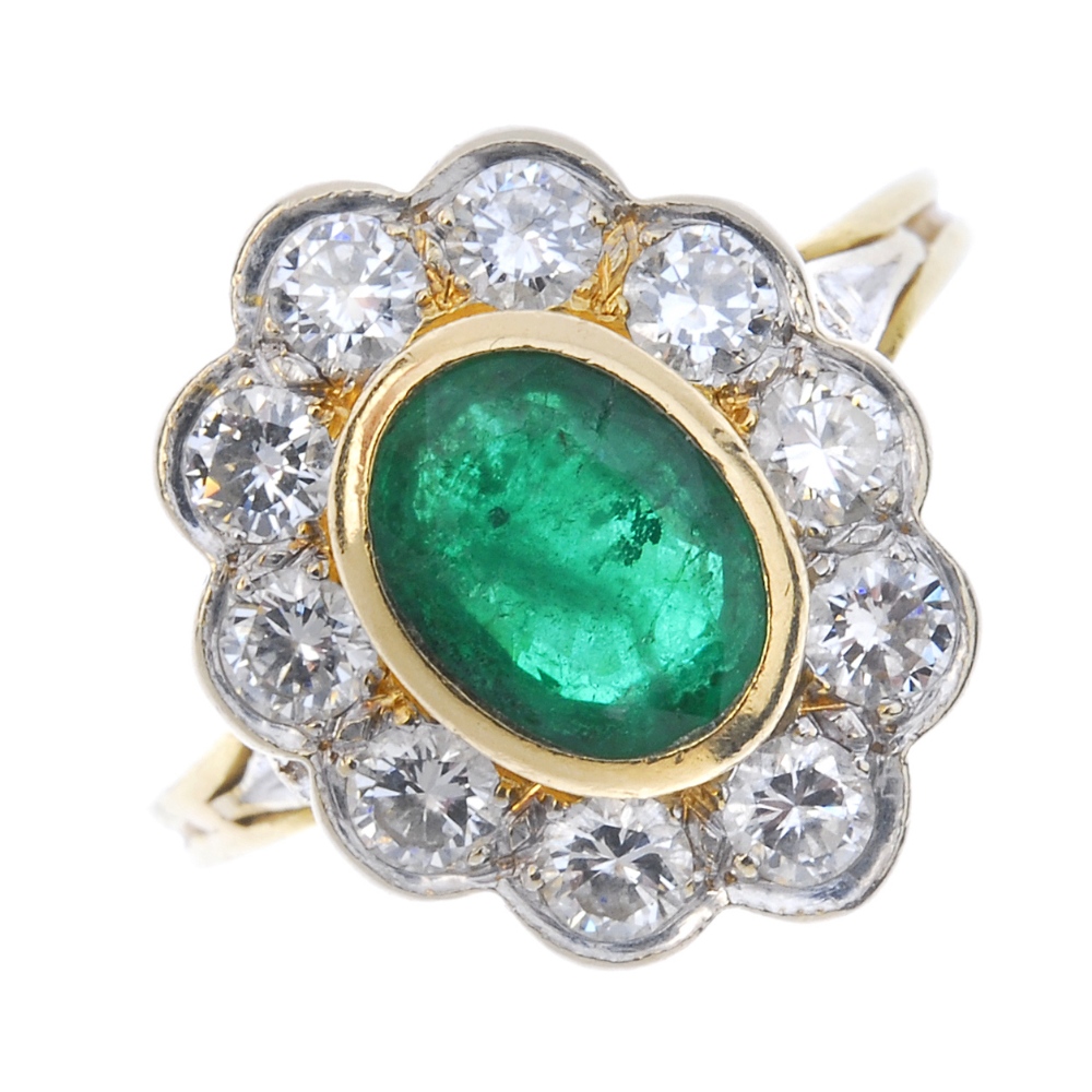 An emerald and diamond cluster ring. The oval-shape emerald collet, within a brilliant-cut diamond