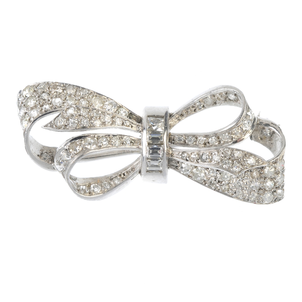 A diamond bow brooch. The brilliant and circular-cut diamond bow, gathered by a tapered baguette-cut